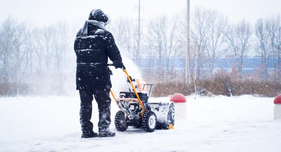 A man cleans snow from sidewalks with snowblower.