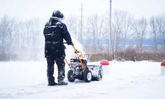 A man cleans snow from sidewalks with snowblower.