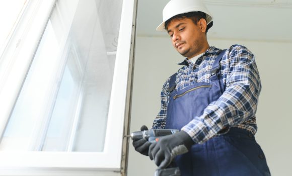 Indian service man installing window with screwdriver.