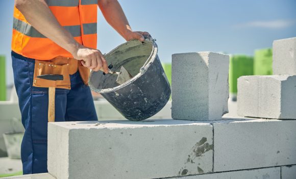 Cropped photo of a bricklayer scooping the mortar with a trowel from a metal bucket