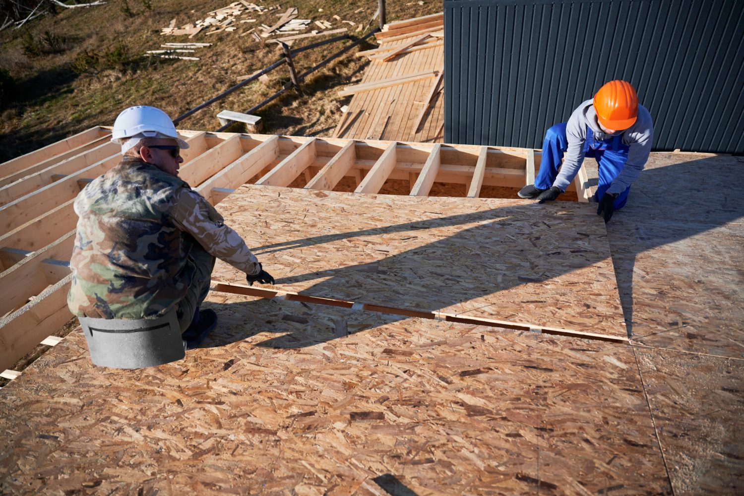 Carpenters mounting wooden OSB board on rooftop of future cottage. Men workers building wooden frame house. Carpentry and construction concept.
