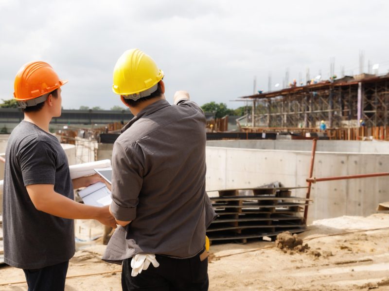 Team of construction workers discussing project details with blueprint in construction site.